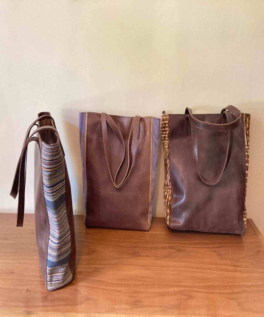 Borsa con pannelli laterali in pelle dalla forma rettangolare strutturata, corpo in pelle liscia e inserti in tessuto testurizzato, progettata in Italia